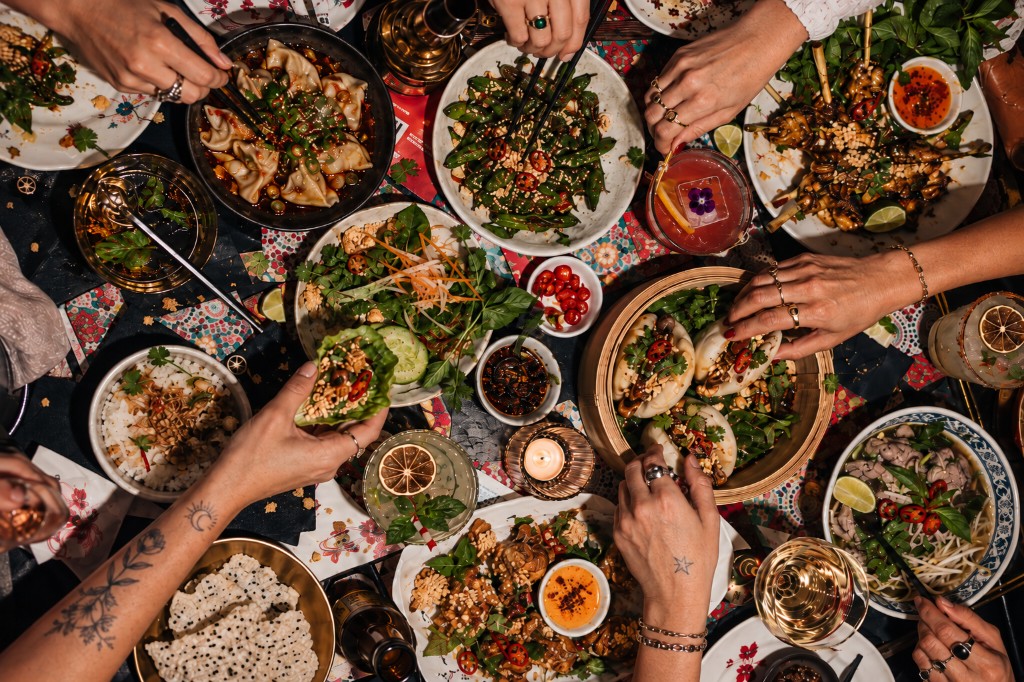 A shared table of dishes, drinks and hands reaching in.